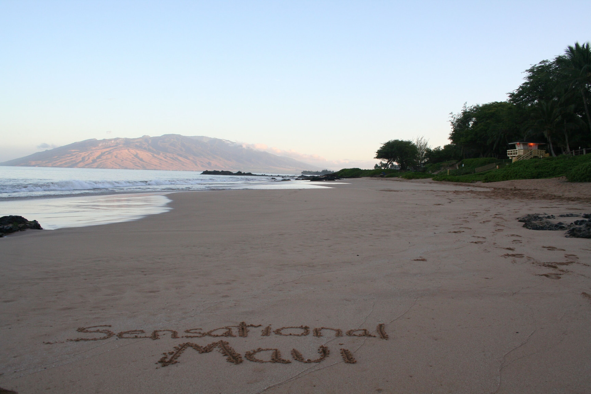 Quiet Maui beach with Sensational Maui written in the sand and the West Maui Mountains beyond